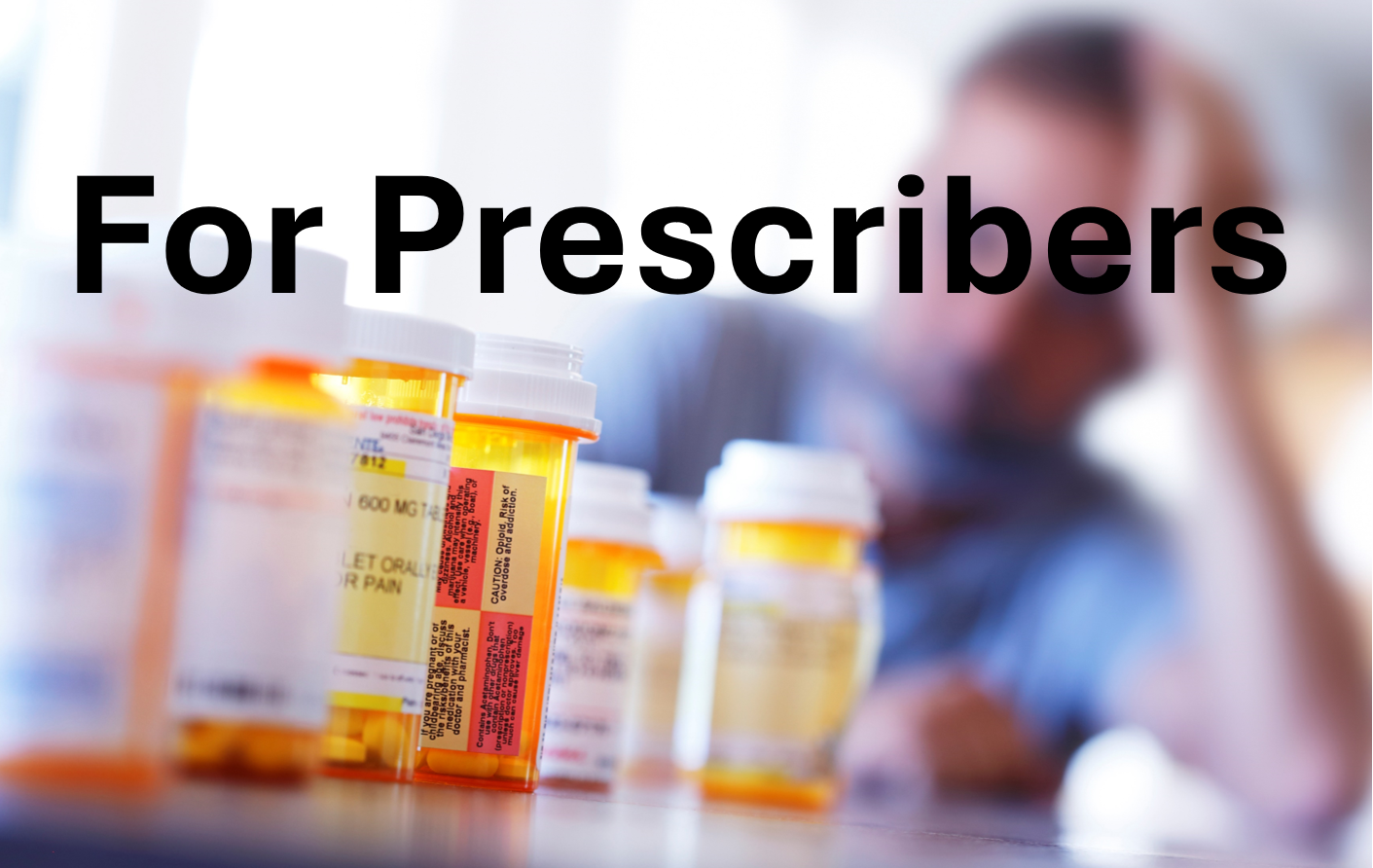text: for Prescribers and image of close up of bottles of pills with a person in the background resting their head on their hand while leaning with their arm on a desk